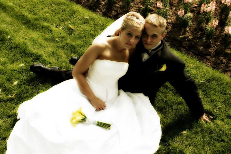 Newlyweds take dramatic photos while sitting in a park in their dress and tuxedo with yellow flowers