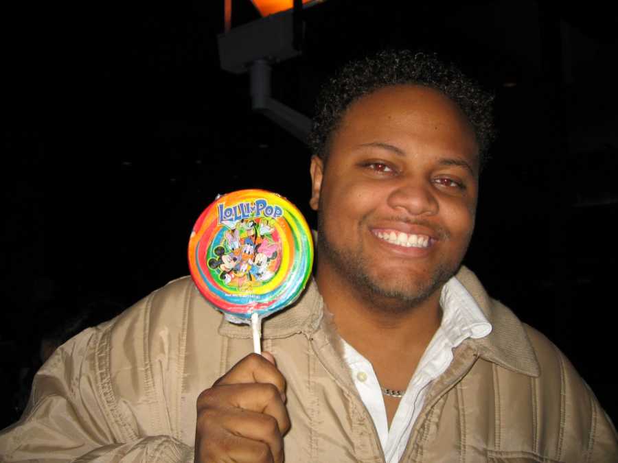 Man battling weight issues smiles for a photo while holding a Disney lollipop