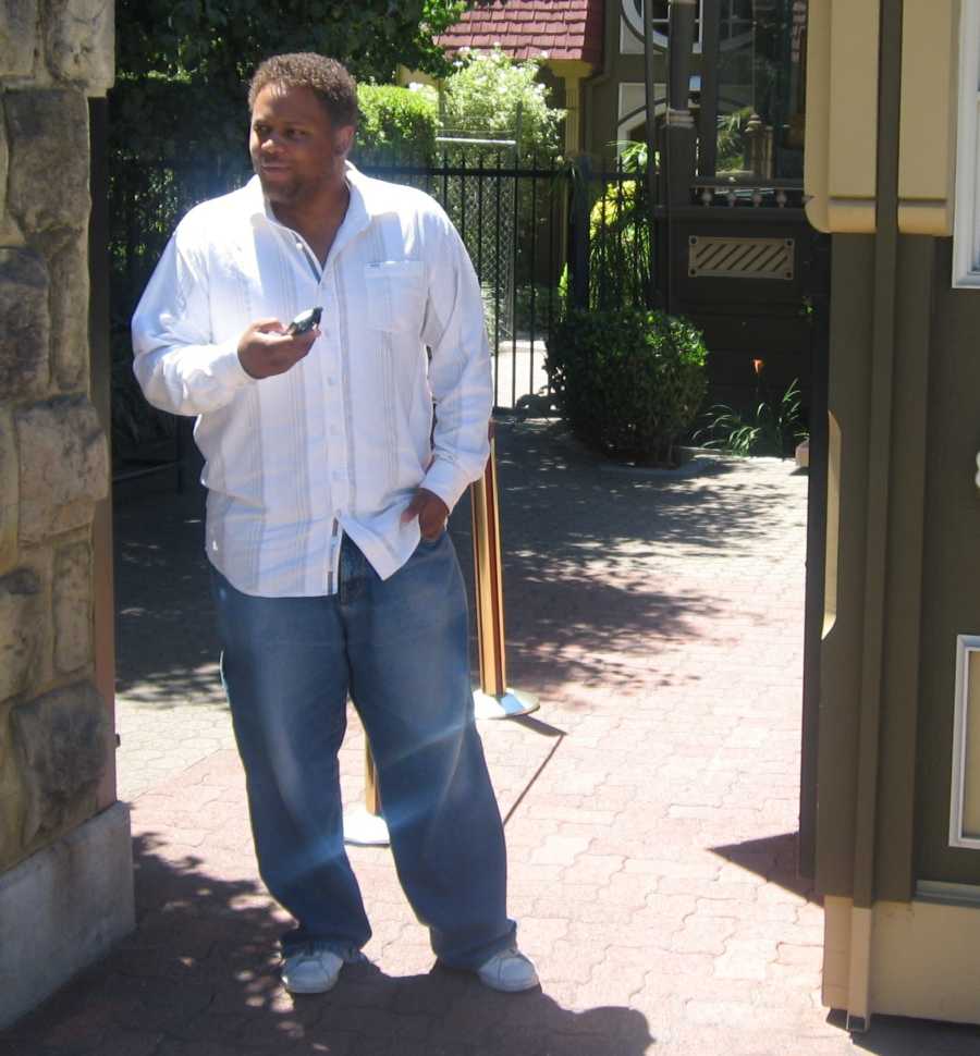 Man stands by a wall in baggie jeans a white long-sleeved button down shirt