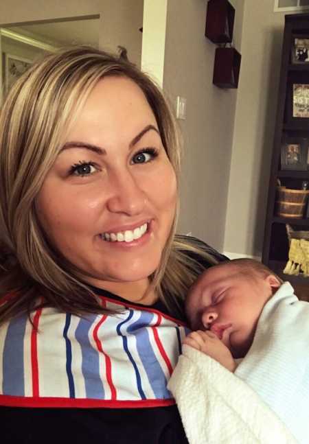 Mom smiles big while holding her sleeping newborn son on her chest