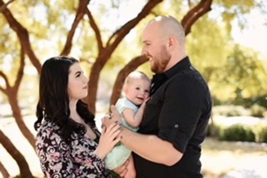 Couple take candid photo looking at one another while holding their daughter between them