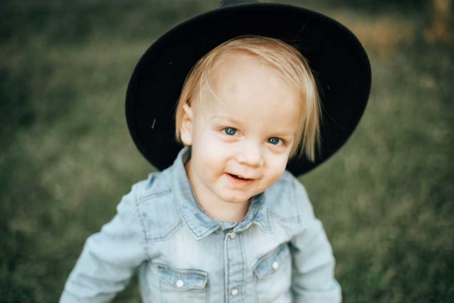 Little girl with blonde hair and blue eyes smile while wearing black hat and blue denim button-down shirt