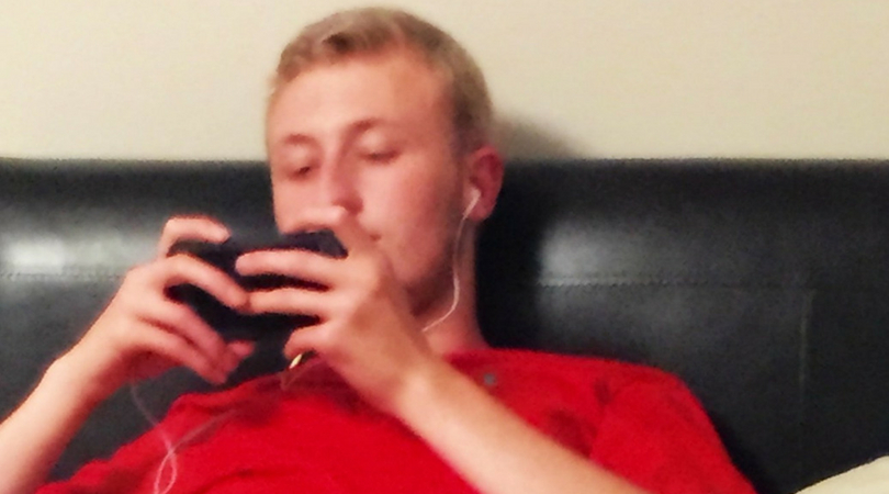 Teen son lays on the couch with headphones in while watching something on his phone