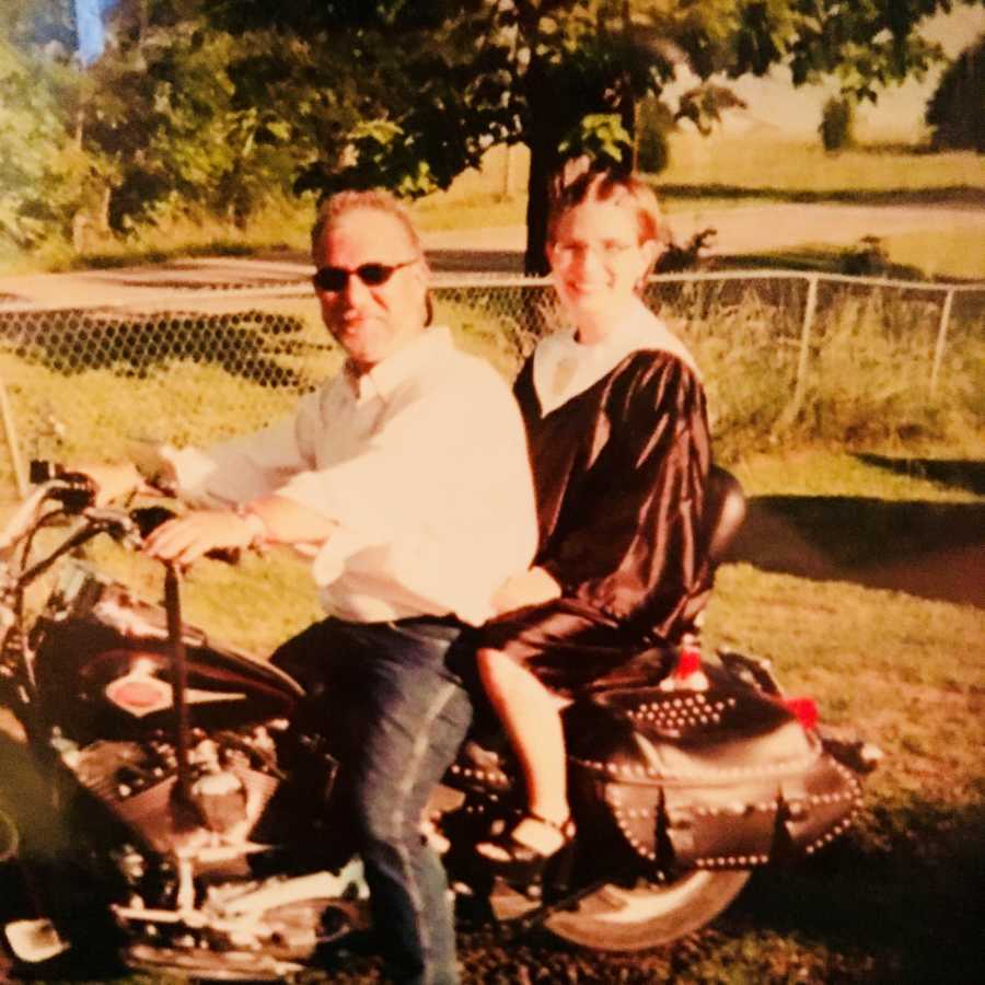 Young girl in graduation gown sits on the back of her dad's motorcycle