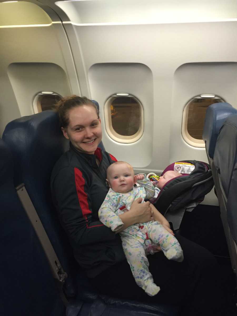 Young mom holds her twin daughters while on an airplane flight