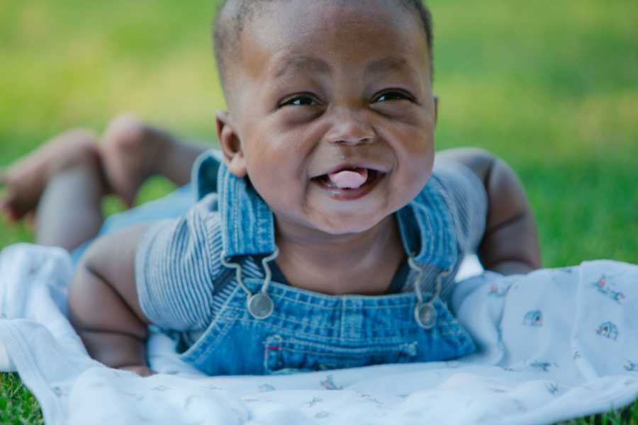 Foster child in blue denim overalls smiling atop blanket