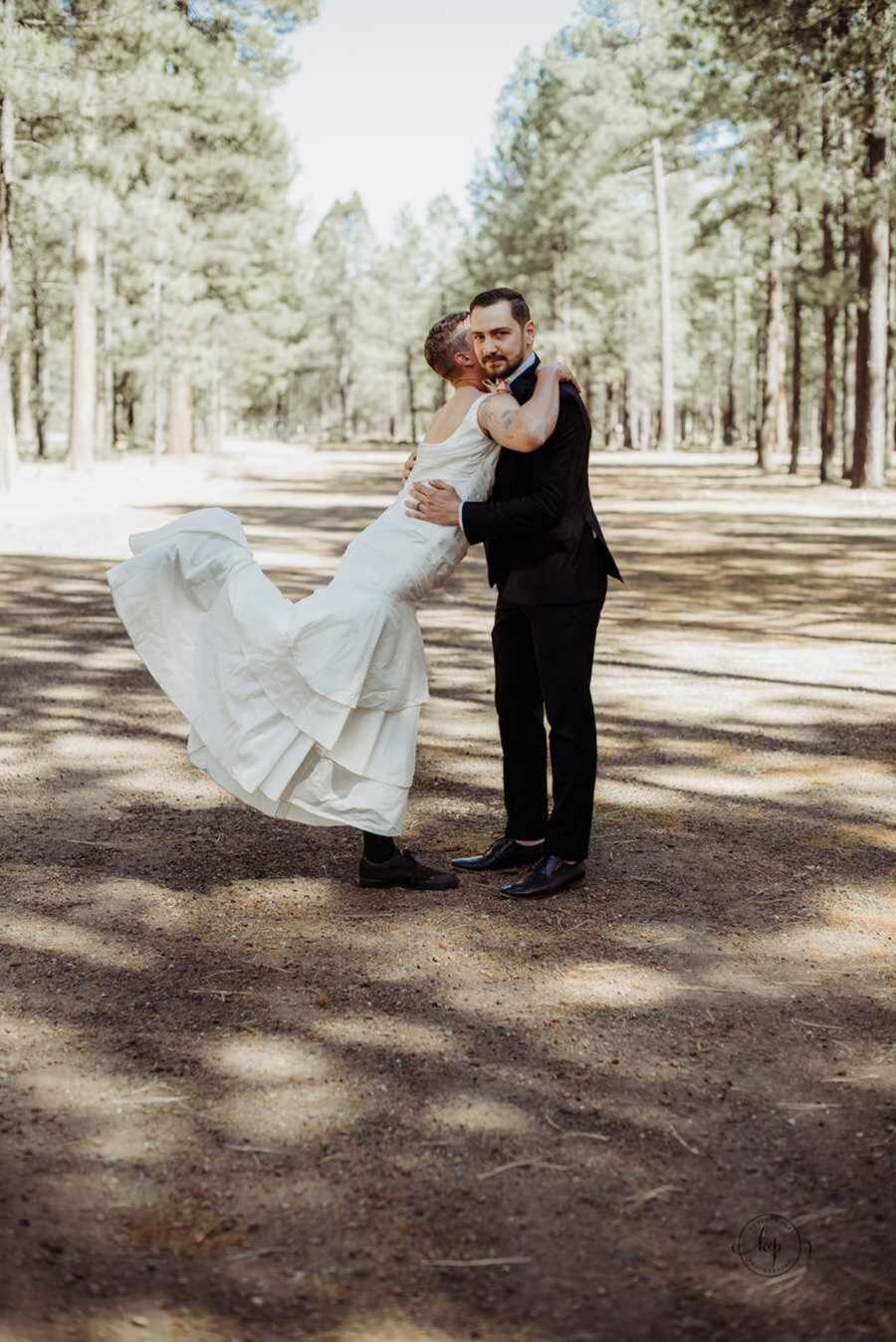 Groom holding best man in wedding dress while he pops his leg up