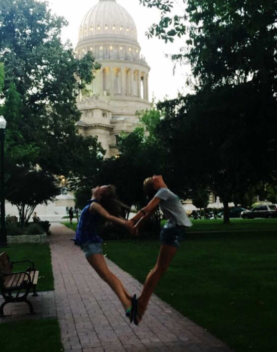 Two daughters jump and make a heart with their bodies with big building behind them