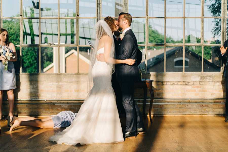 Couple kiss after saying "I do" while the bride's sister lays on the floor after passing out in the greenhouse