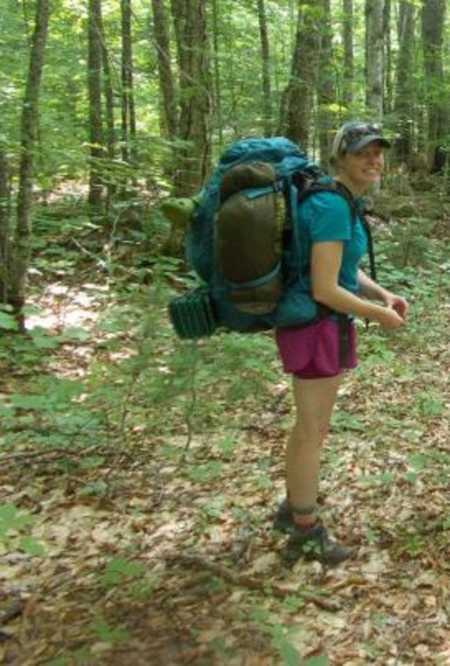 Woman smiles for a photo while hiking in a forest