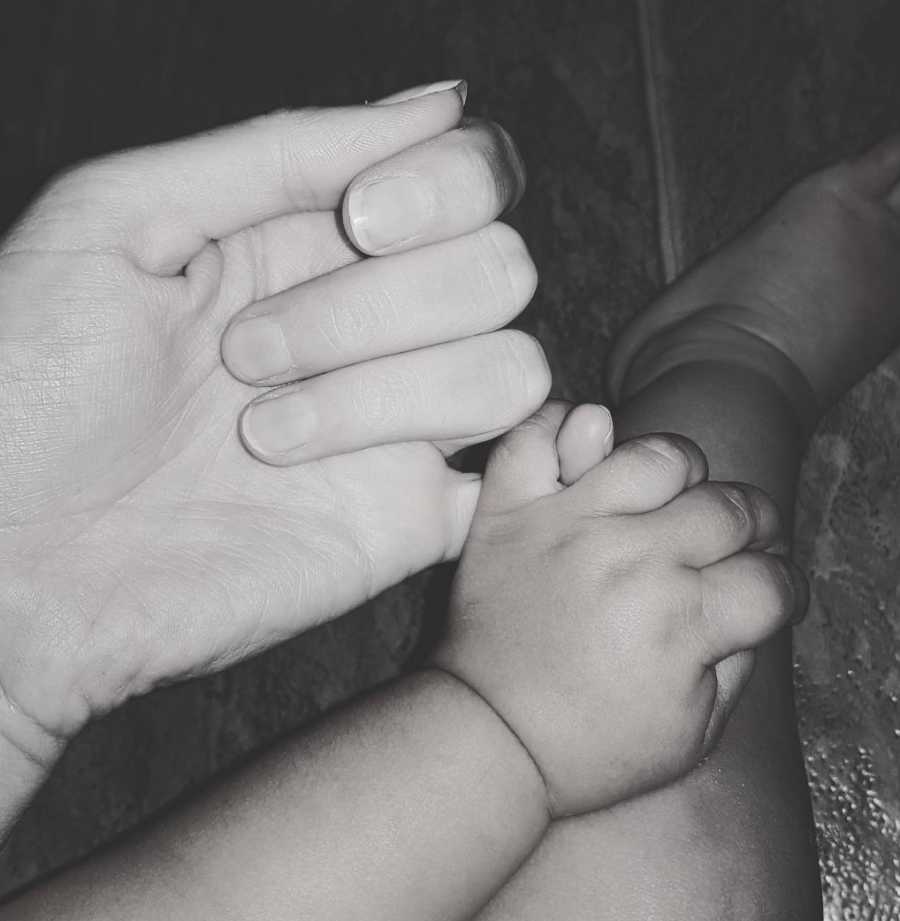 Foster mom holds pinkies with her young foster son while cuddling