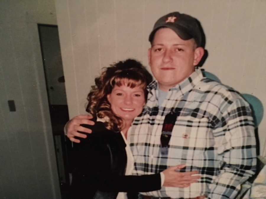 Mom hugs her grown son while they both look into the camera for a photo