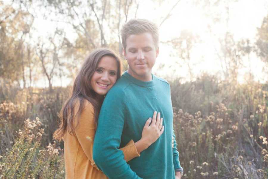 Couple experiencing infertility take a photo together during an outdoor photoshoot, she in a yellow sweater and him in a green long-sleeved shirt
