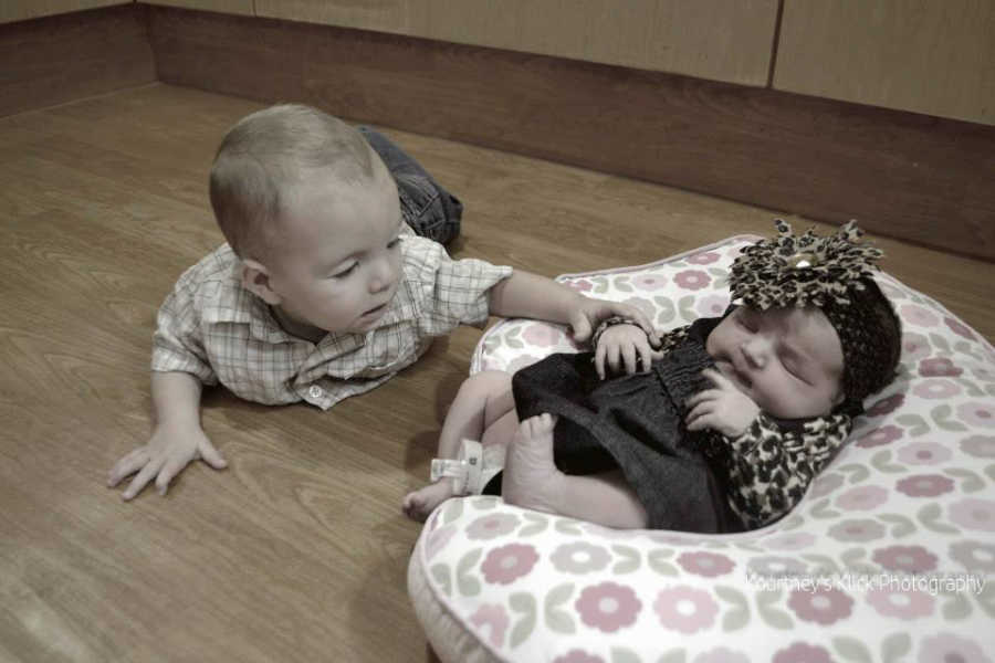 Infant with chromosome 7 inversion lies on ground touching newborn sister who is sleeping