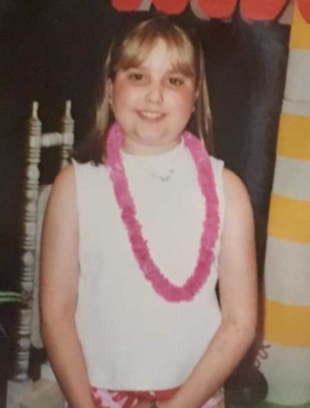 Young girl with crohn's disease stands with pink lei around her neck