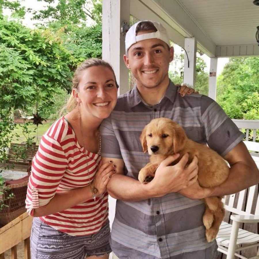 Young couple standing on porch smiling with puppy
