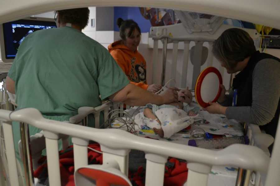 Baby with chromosome 7 inversion lying in hospital with mother and nurse over him and doctor giving x-ray