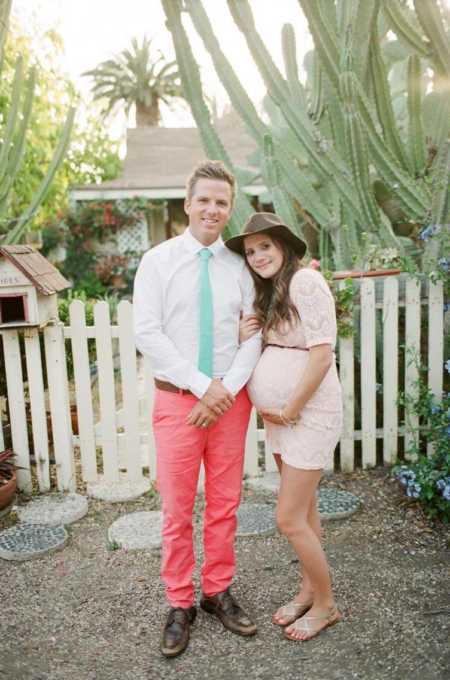 Husband and pregnant wife who make an effort with each others parents stand smiling outside of house