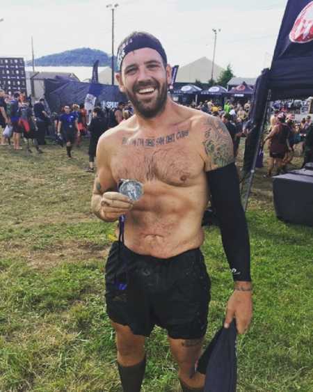 Man who was once and alcoholic and overweight standing holding medal after completing Spartan race