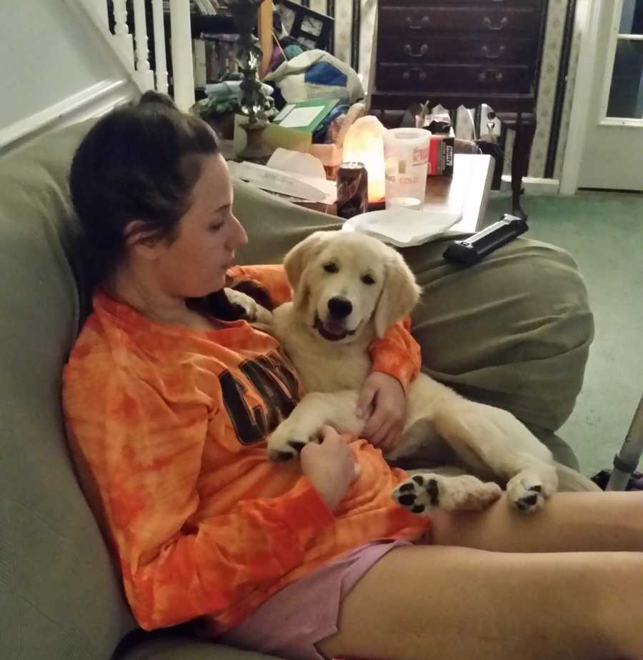 25 year old sitting on couch at home with golden retriever puppy who would help her recover