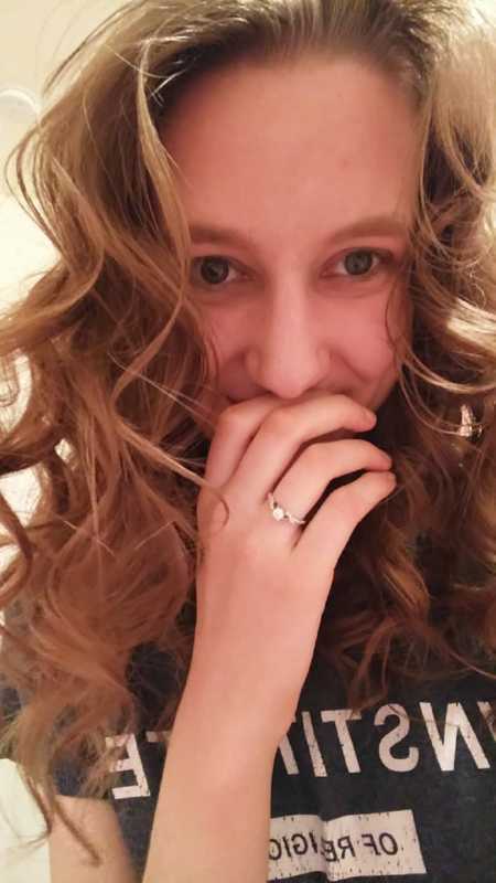 Woman smiling with hand to her mouth with engagement ring on in selfie