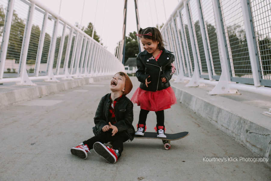 Toddler with chromosome 7 inversion sits on skateboard smiling while younger sister stands on skateboard