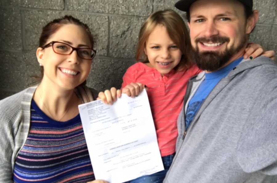 Couple take a photo with their adopted daughter and her adoption papers