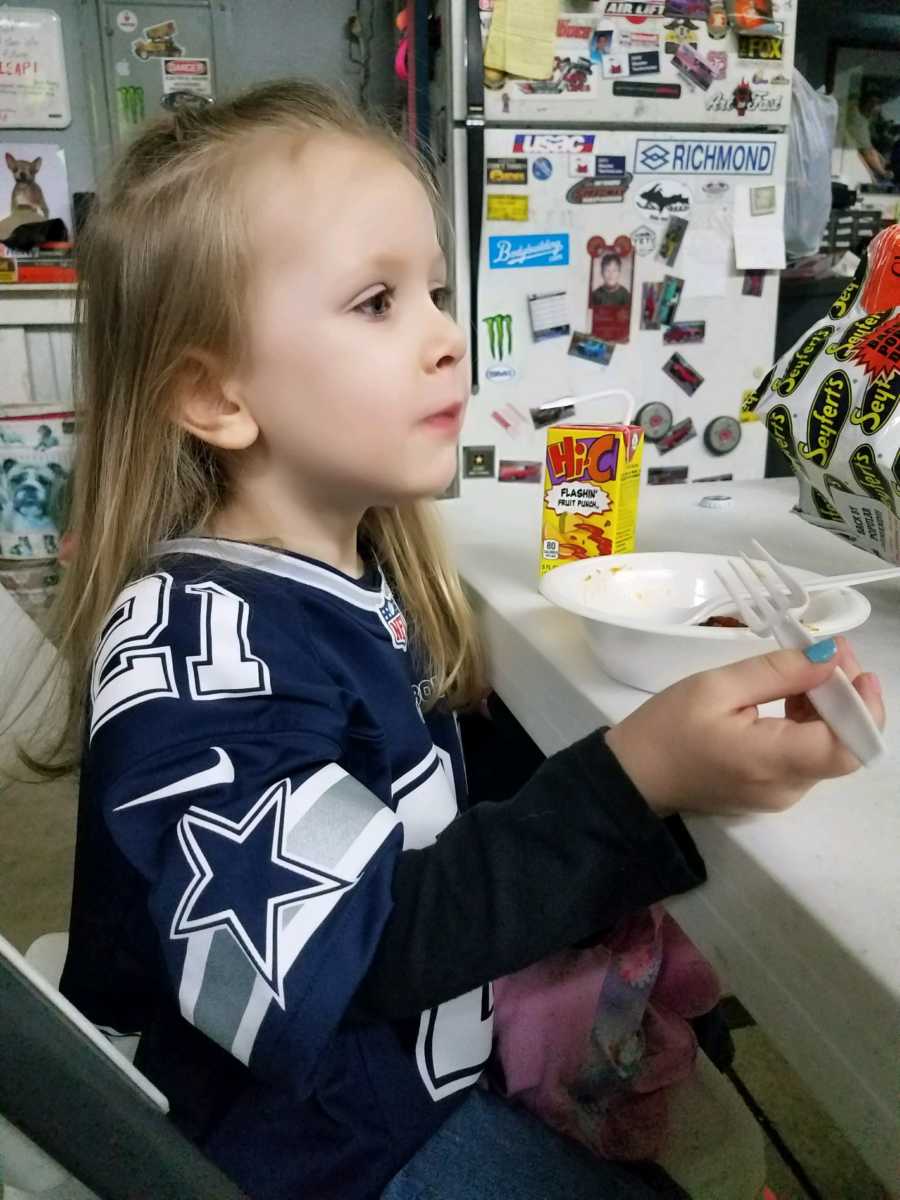 Little girl sits at table in Dallas Cowboys jersey eating food