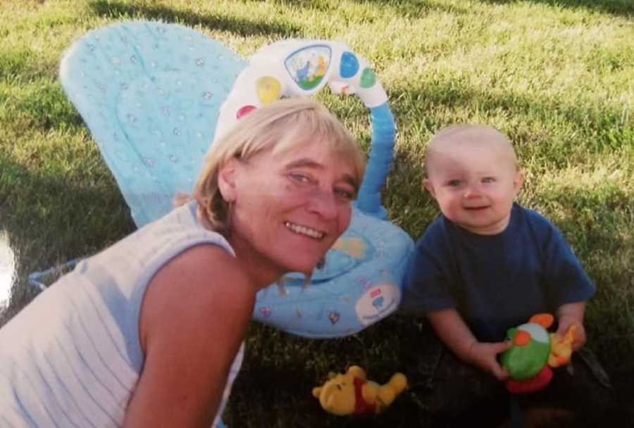 Birth mother of woman put up for adoption sits in grass with biological son who plays with toys