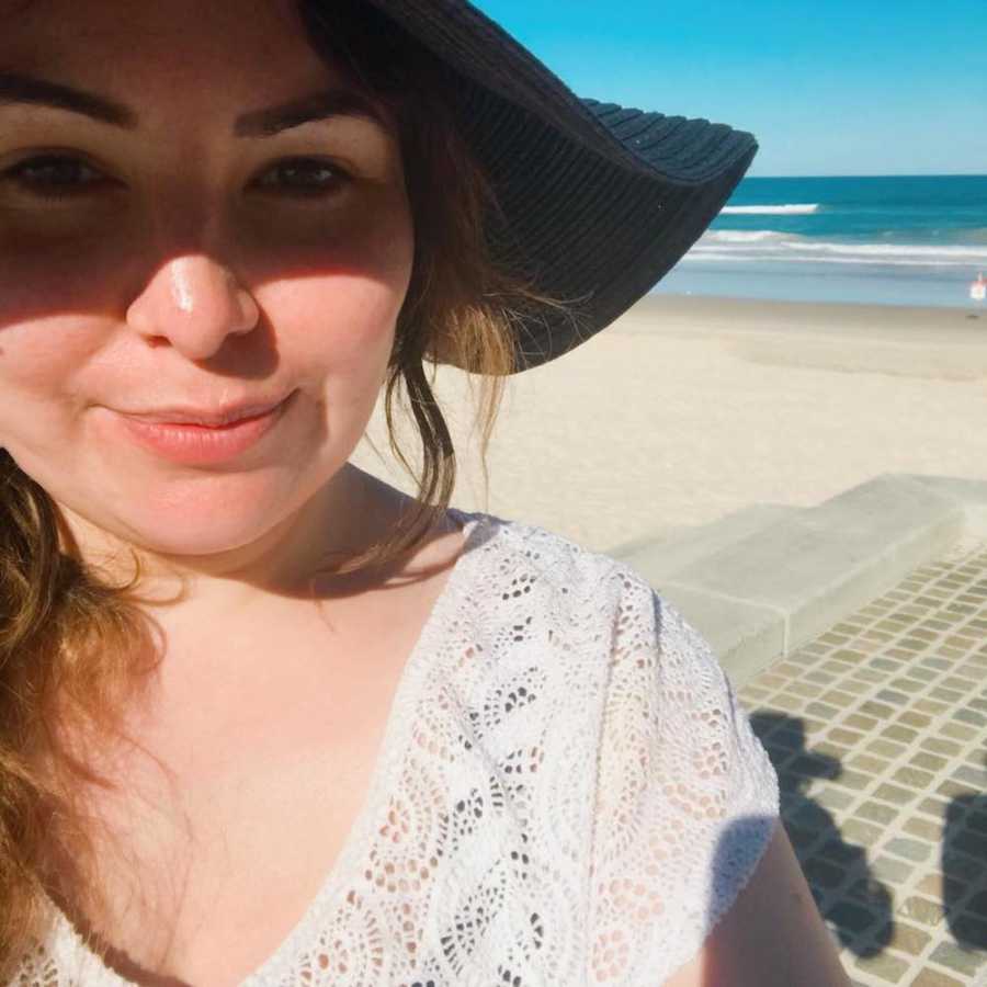 Mom takes a selfie on the beach in a sunhat with the water behind her