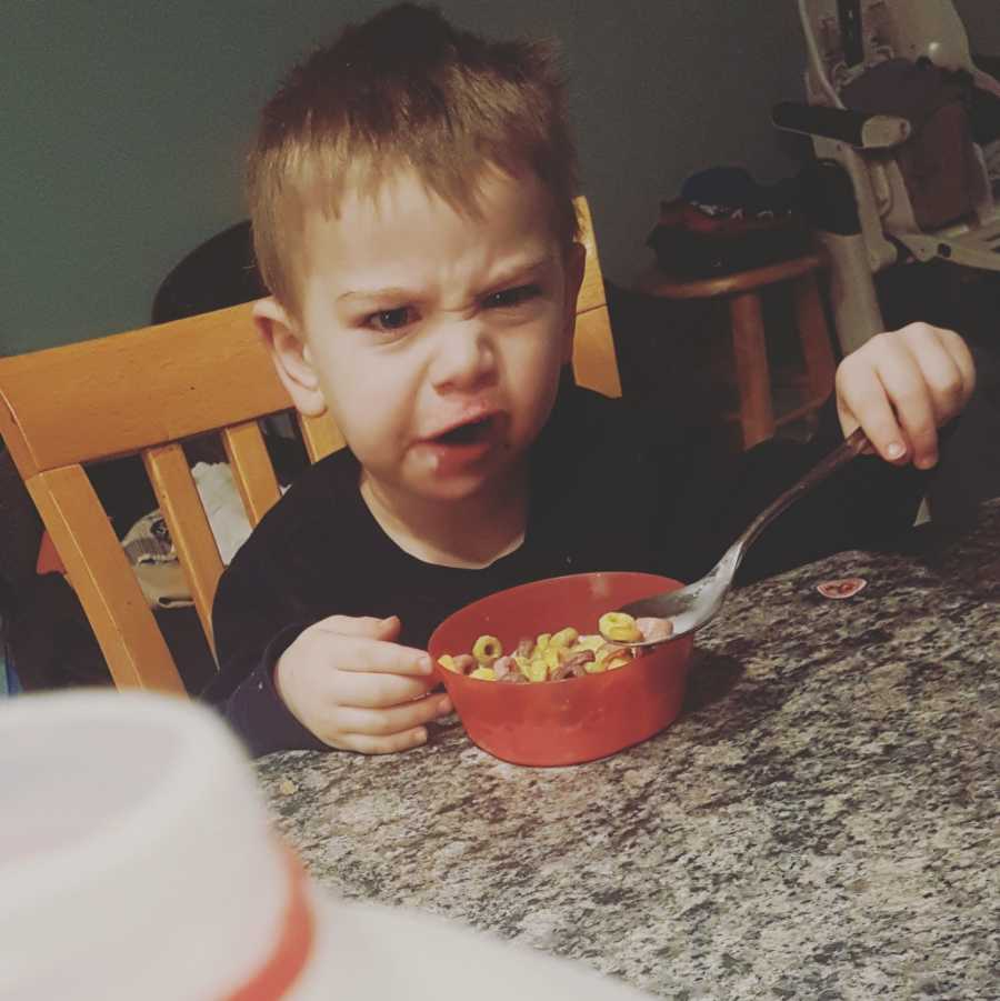 Angry toddler eats cereal at table who mother feels stressed 