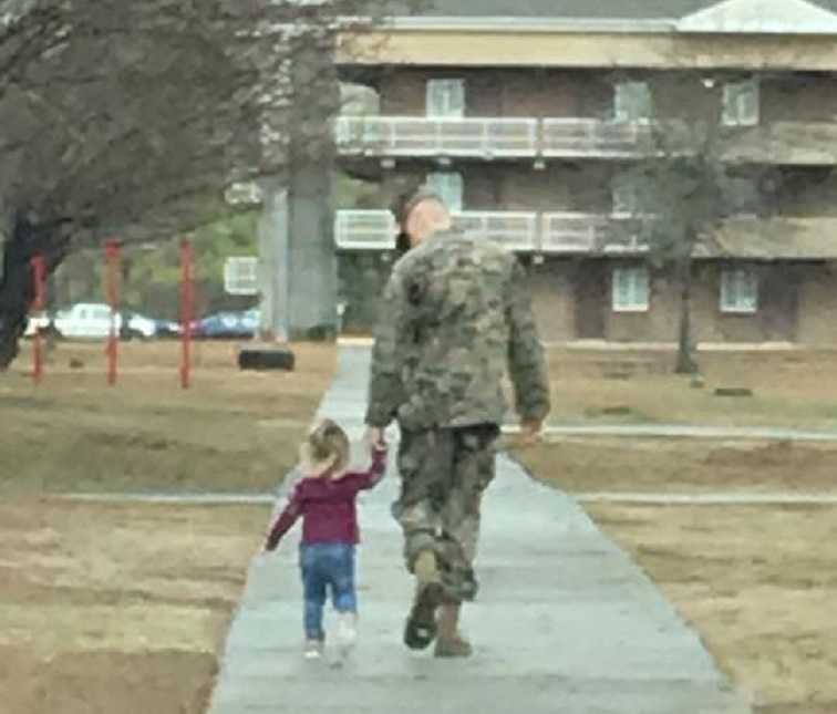 Little girl who has special relationship with soldier father walks with him hand in hand down sidewalk