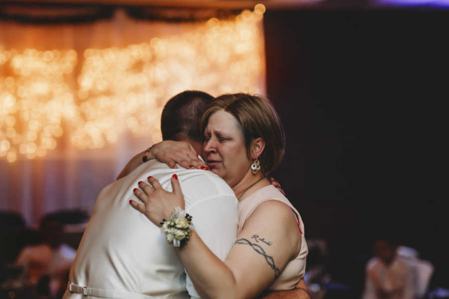 Groom and mother with breast cancer hug at wedding