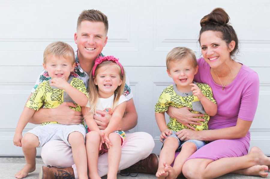 Mother who was overwhelmed when husband went back to work sits on ground beside husband with their triplets