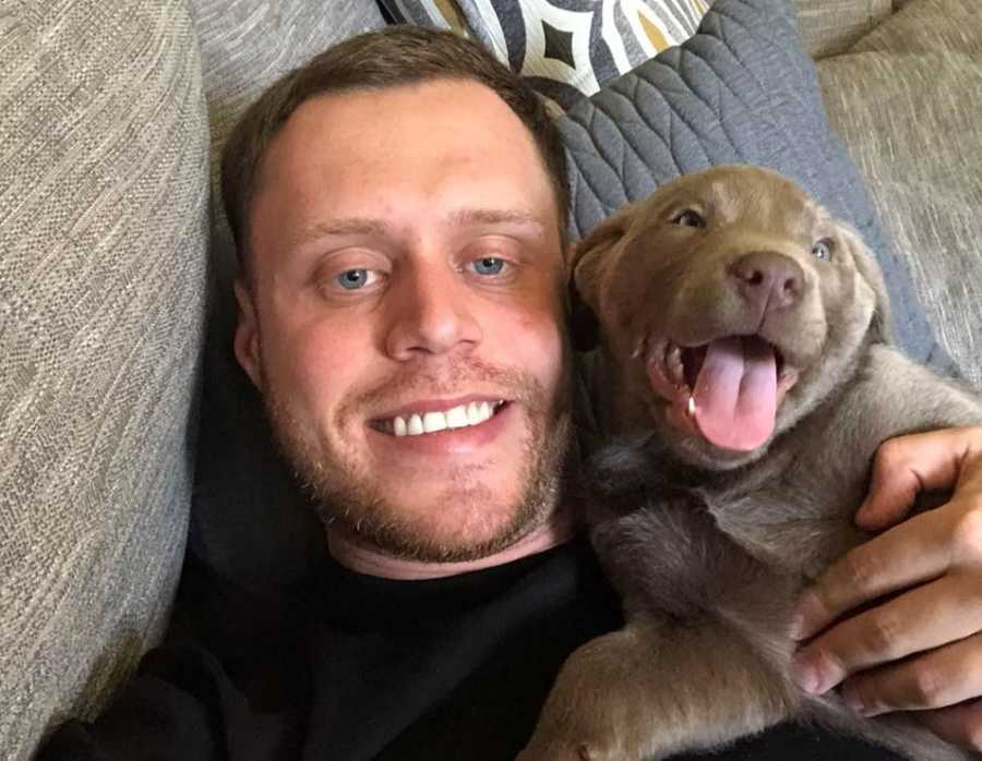 Man who got clean smiles laying on couch with puppy beside him