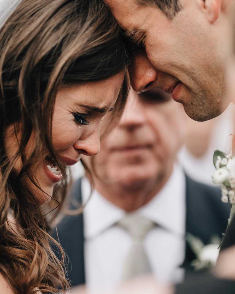 Bride sobs as she rests her head against groom's at wedding