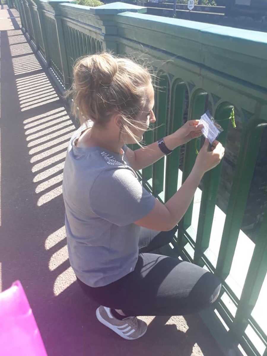 Woman bends down to read note attached to bridge
