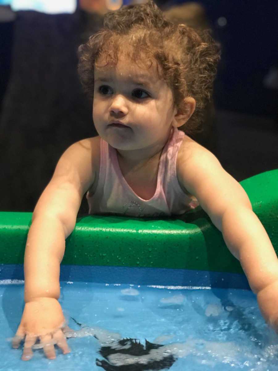 Young child with hands in water whose mother urges people to stop asking her how much her daughter weighs