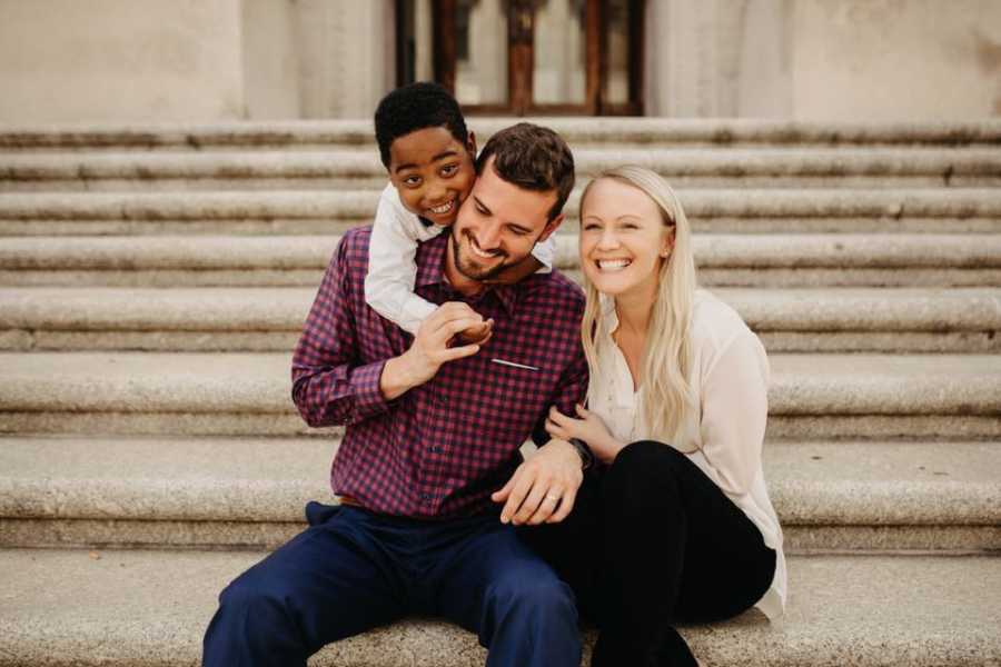 Husband and wife sit on steps outside of adoption court with their son on fathers back