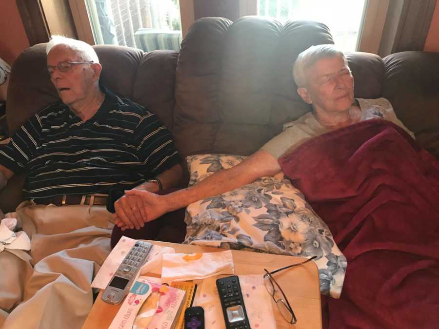 Woman with dementia holds her husband's hand while they sit on the couch together