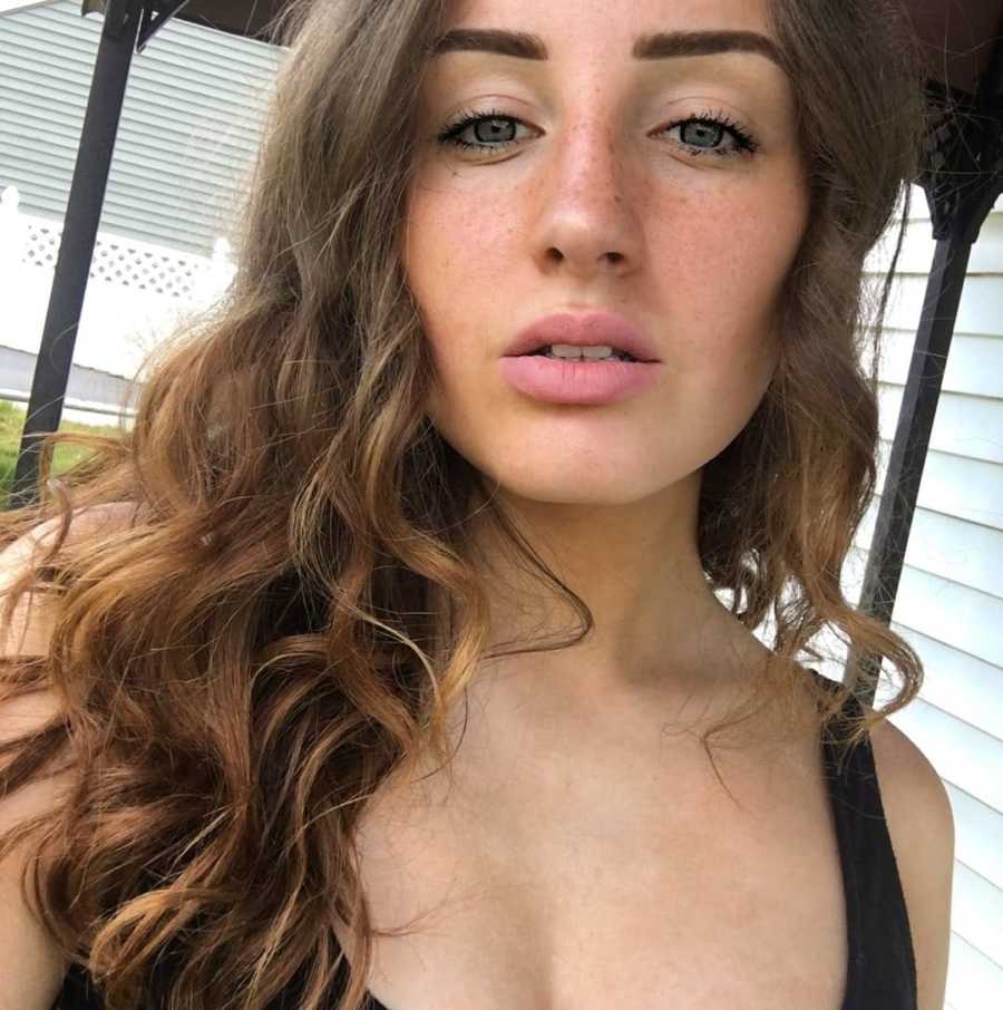 Woman with brown curly hair takes a selfie while making a pouty face