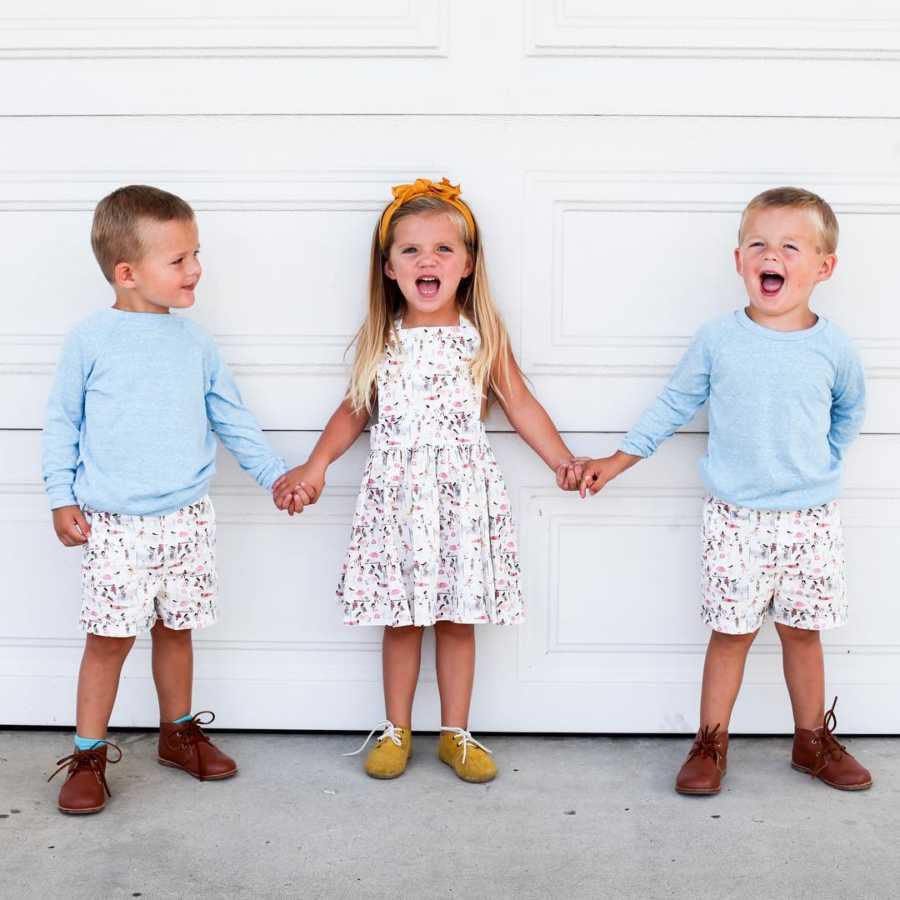 Triplets whose mother felt overwhelmed when husband went back to work, stand holding hands in front of garage