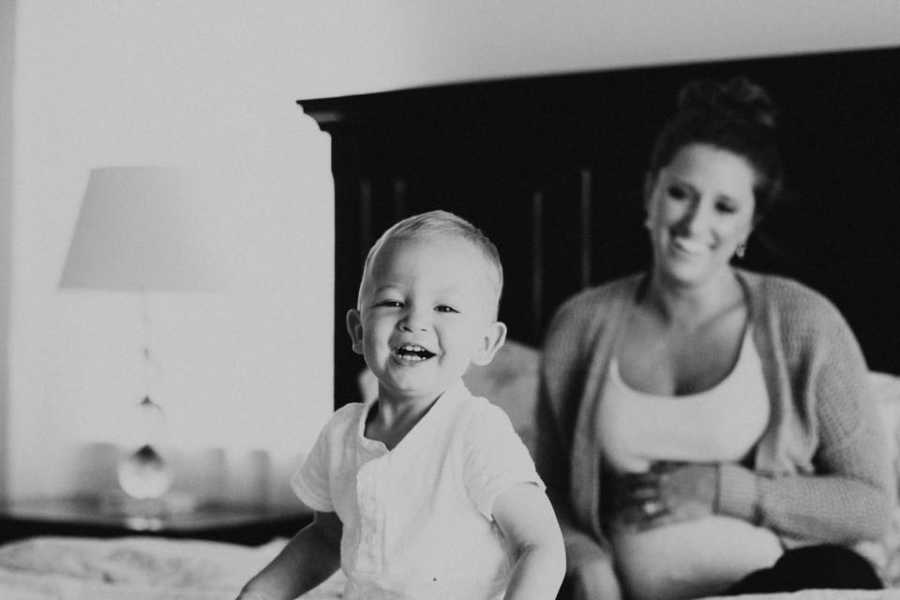 Toddler who mother writes letter to sitting on bed smiling with pregnant mother behind him