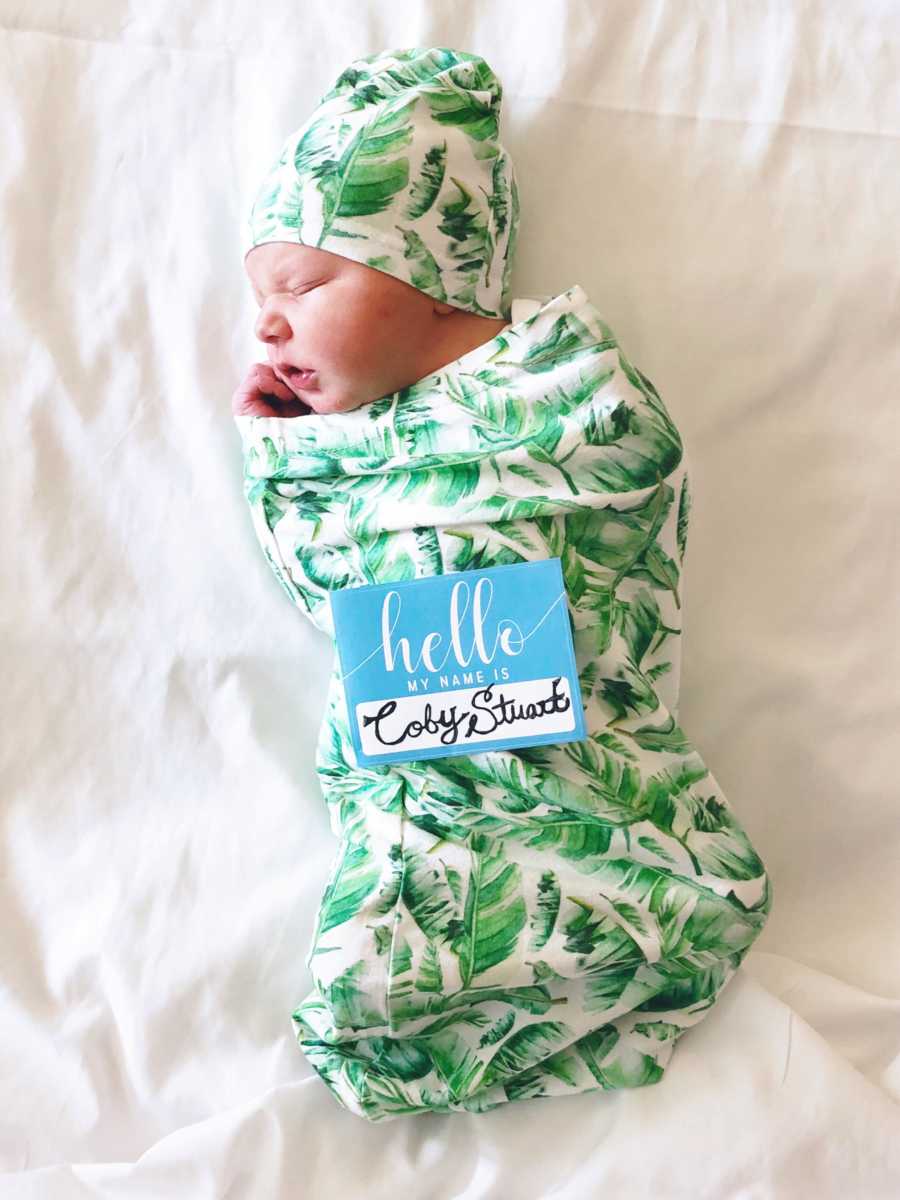 Newborn boy sleeps in leaf-patterned swaddle with matching beanie