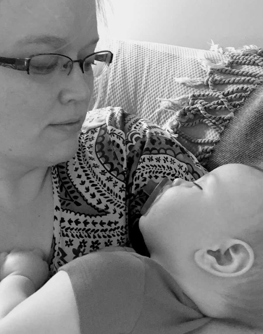Mom looks down at her newborn sleeping in her arms with a pacifier in his mouth