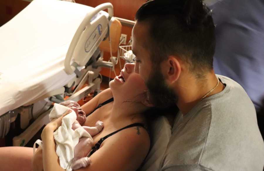 Woman cries while holding her newborn child while her husband holds her
