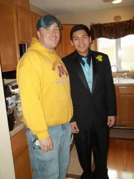 Foster son wears a suit before a school dance and takes a photo with his foster dad in their kitchen