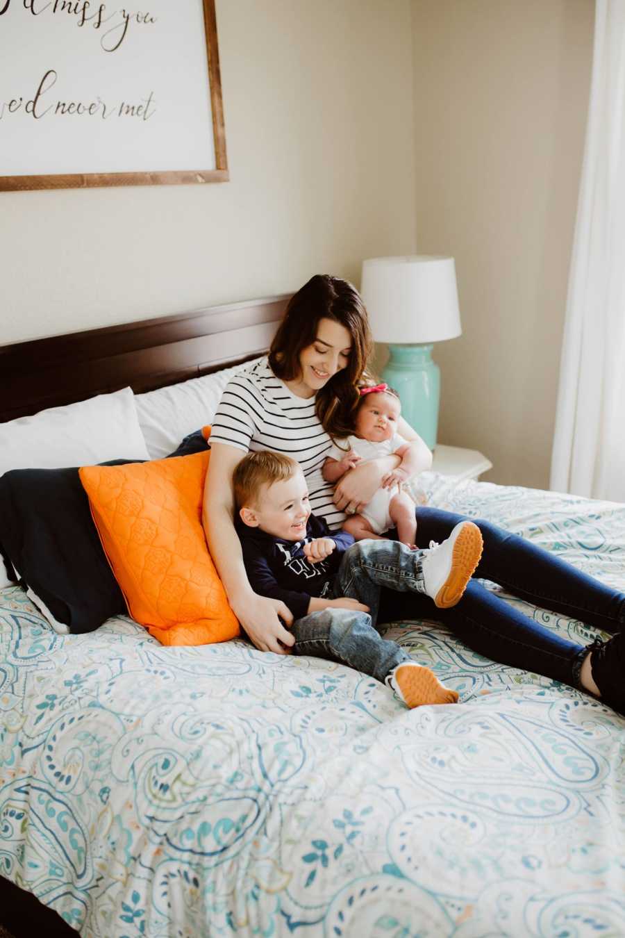 Marine wife and mom of two smiles for a candid photo with her two babies in bed with her