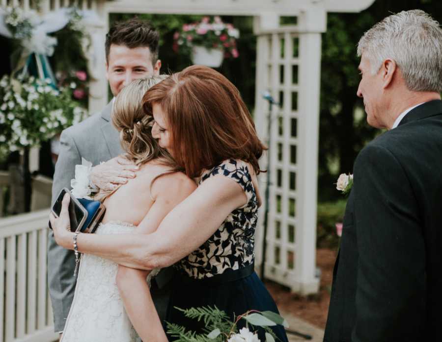 Bride with crohn's disease receives hug from mother while groom and father watch