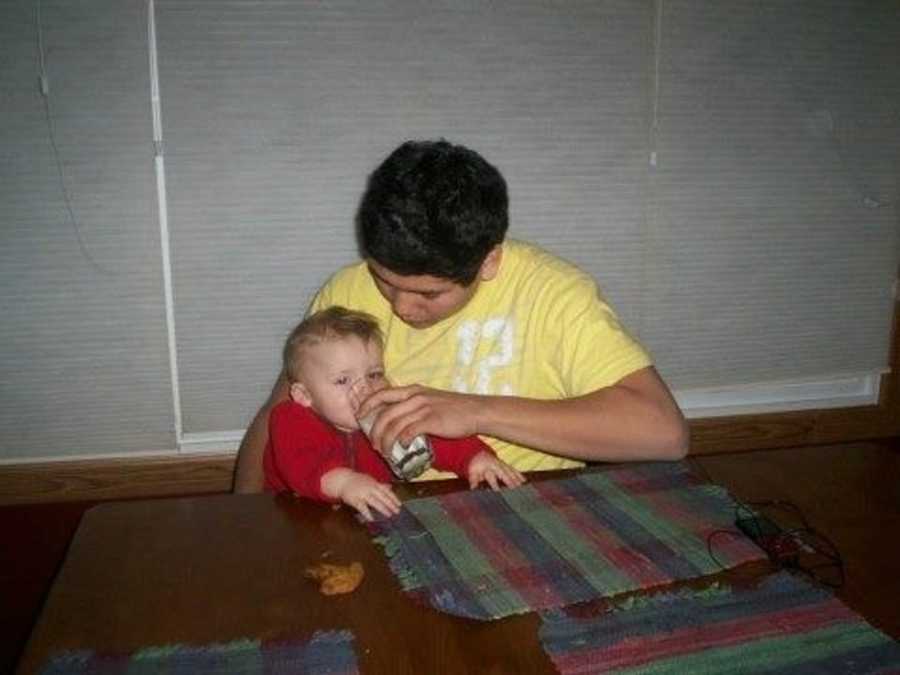 Foster son sits at the dining table and helps his little brother drink a glass of milk